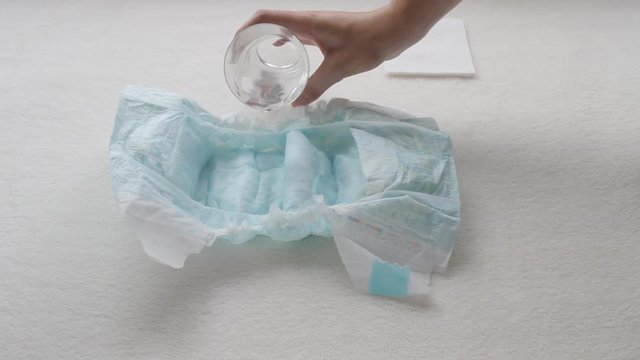 Girl pours water from a glass in a children's diaper, close-up, diapers and water