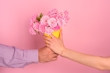 Man giving flower present to woman. Two people hold flower bouquet on pink background in studio. Conсept of small present to beloved girlfriend. Pleasant surprise for female. Date and pink flowers
