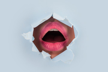 Surprise. Female mouth in colored with pink lipstick is through hole in paper. Seductive female mouth is open in torn paper. Women sexy mouth inside. Scream and the right to vote. Feminism and voting