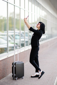 Young pretty girl dressed in a business suit and in the glasses with a suitcase talking on the phone and photographed