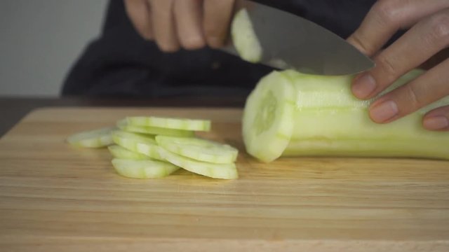 Slow motion - Close up of chief woman making salad healthy food and chopping cucumber on cutting board in the kitchen.
