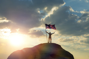 the man is standing on the top of the mountain, holding his hands up with the flag of the US...