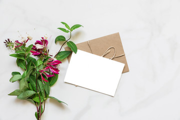 blank white greeting card with pink honeysuckle flowers bouquet over white marble table with copy space. top view