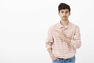 Sad news got man upset. Gloomy tired caucasian european man with beard and moustache, pointing at upper left corner, retelling horible event that happened to friend, standing over gray wall