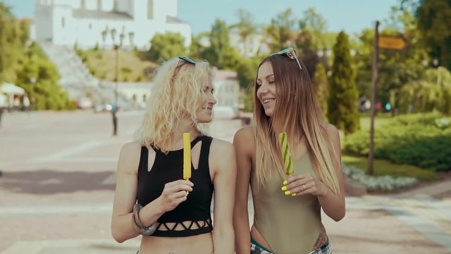 Beautiful women friends walking in city street eat ice cream in slow motion.