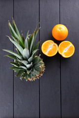 Pineapple and oranges on wooden boards, pineapple with leaves and halves of oranges on a black background, citrus with copy space, blank for designer, vegetarian tropical food, top view