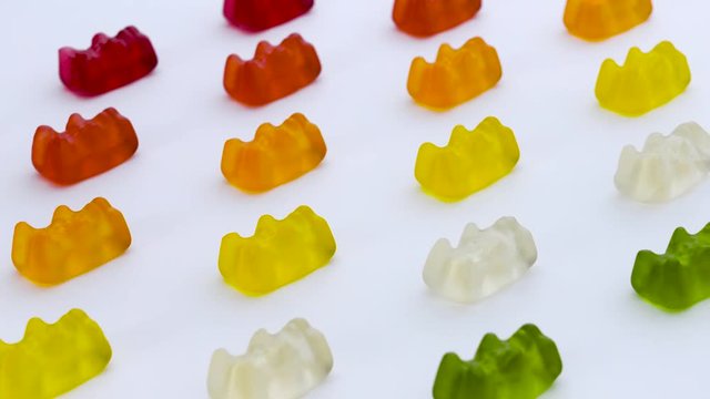 Gold bears. Colorful animal gummy candies rows are moving diagonally on the white background.