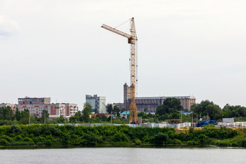 Fototapeta na wymiar high-rise construction crane on the river Bank at the construction site fence