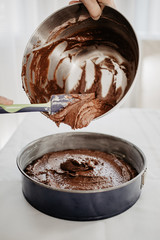 Chocolate cake dough being transferred into round-shaped baking tin with silicone spatula. Woman...