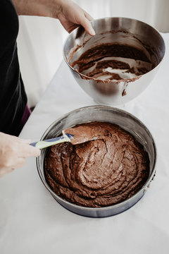 Chocolate Cake Dough Being Transferred Into Round-shaped Baking Tin With Silicone Spatula. Woman Preparing Chocolate Cake To Be Baked. White Background.