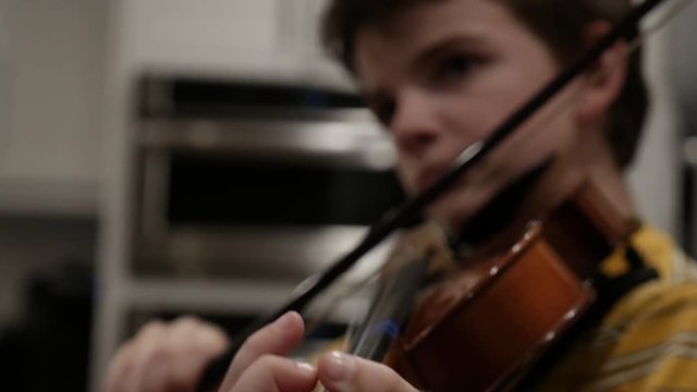 Young 10 - 12 year old boy practicing violin in a modern kitchen
