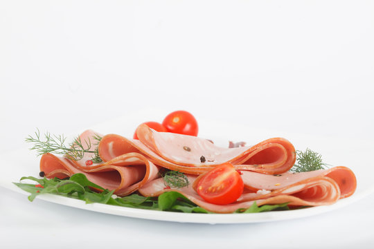 Italian mortadella on white plate with tomato and red and black pepper. Bologna salami for appetizer.
