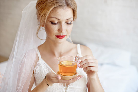 Close-up blonde bride drinking morning tea in lingerie and veil.