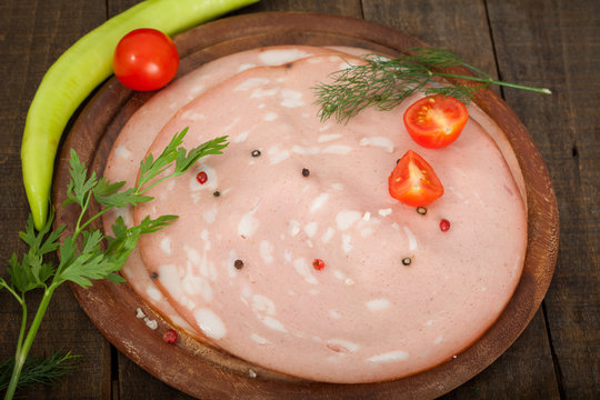 Slices of freshly cut mortadella slices on a wooden board. Italian Bologne salami with red and black pepper.