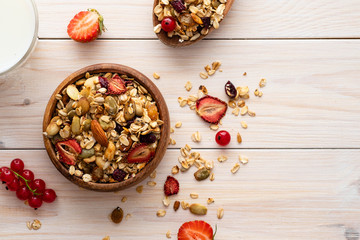 Bowl of oat granola, fresh raspberries, blueberries and nuts on white wooden board for healthy breakfast. top view