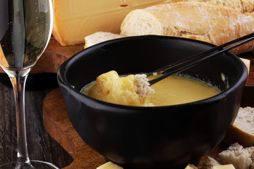 Gourmet Swiss fondue dinner on a winter evening with assorted cheeses on a board alongside a heated pot of cheese fondue with two forks dipping bread and white wine behind in a tavern or restaurant