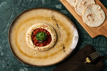 Easy Hummus with harissa sauce and pistachios, close-up. Vegetarian diet food with pita bread on wooden cutting board, top view. 