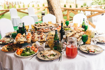 Festive rich round table with white tablecloth and chairs, served with a variety of delicious dishes, original snacks and drinks. Buffet in nature