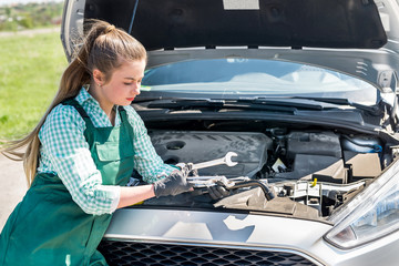 Young mechanic with different wrenches and spanners before car