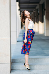 Stylish woman jumping in the street. Fashion portrait of beautiful woman in the street, urban background. Woman portrait outdoors in floral skirt and white top.