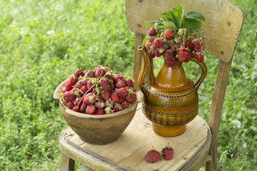 Old clay pot full of fresh red strawberries and ceramic decorative jug with strawberries on the chair