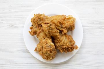Fried chicken legs on a white plate over white wooden background, close-up. Top view, from above.