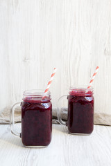 Glass jars with berry smoothie on white wooden background, side view. Space for text.