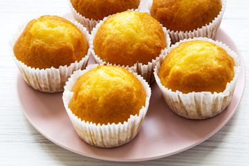 Fresh tasty cupcakes on pink plate over white wooden surface, side view. Close-up.