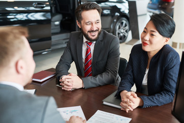 Smiling business colleagues sitting at the table and discussing contract at auto salon