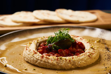 Delicious Hummus with harissa sauce and pistachios, close-up. Vegetarian diet food with pita bread on wooden cutting board