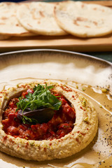 Delicious Hummus with harissa sauce and pistachios, close-up. Vegetarian diet food with pita bread on wooden cutting board