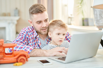 Warm toned portrait of handsome father teaching son how to use laptop or playing computer games together
