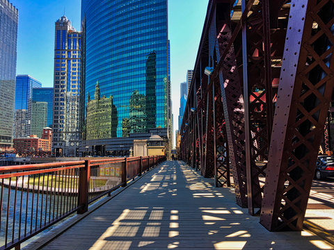 Chicago's elevated train tracks cast shadows on Lake Street and sidewalk along the river in downtown Loop.