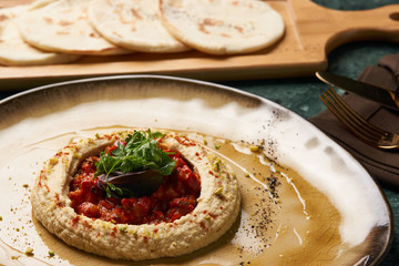 Vegetarian Hummus with harissa sauce and pistachios close-up. Delicious diet food with pita bread on wooden cutting board