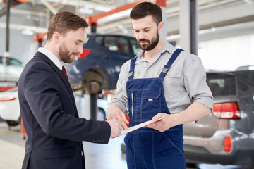 Waist up portrait of handsome businessman signing contract for car repairs while talking to modern...