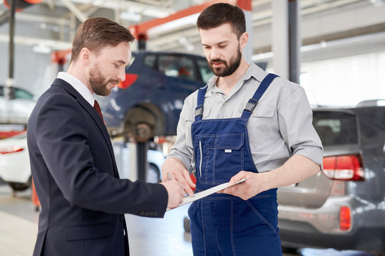 Waist up portrait of handsome businessman signing contract for car repairs while talking to modern mechanic in service garage