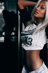 Sexy blonde in shorts and a topic.Blonde on a black background.Girl posing near black fridge door.