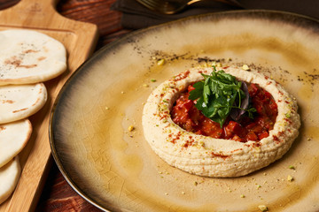 Hummus with harissa sauce and pistachios, close-up. Vegetarian diet food with pita bread on wooden cutting board, top view. 