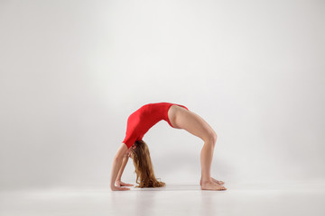 young woman in red leotard balancing on hands and knees and holding back in form of arch while...