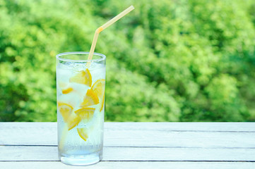 A sweaty glass with a refreshing cocktail with ice and lemon. On a wooden background.