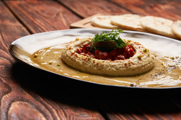 Hummus National Israeli cuisine. Hummus with harissa sauce and pistachios, close-up. Vegetarian diet food with pita bread on wooden cutting board.