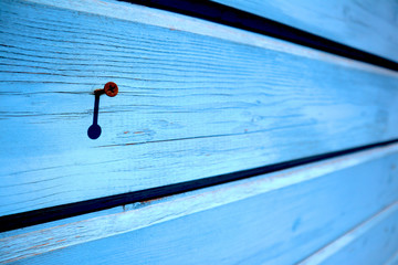 Wooden wall of blue painted planks with single rusty clogged screw, may be used as background