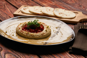 Hummus National Israeli cuisine. Hummus with harissa sauce and pistachios, close-up. Vegetarian diet food with pita bread on wooden cutting board.