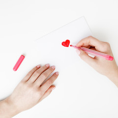 Flat lay. Top view. Hand of girl writing love letter on Saint Valentines Day. Handmade postcard with red heart shaped figure. Woman write Love on postcard for 14 February holiday celebration