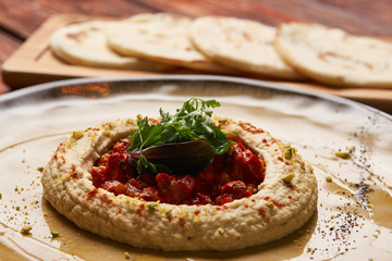 Hummus National Israeli cuisine. Hummus with harissa sauce and pistachios, close-up. Vegetarian diet food with pita bread on wooden cutting board.
