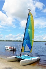 Small sailing catamaran resting on the beach and a small motor boat anchored in shallow water on Sandpiper Bay,St.Lucie River in Central ,Florida