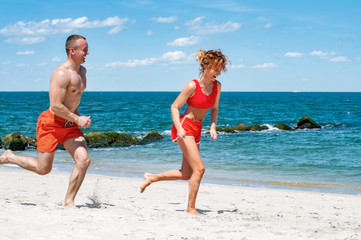 Happy couple running on beach. Man and woman jogging on the sea shore.