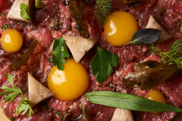 Steak tartare with egg yolk, pistachios, truffle oil, green mayonnaise on luxury porcelain plate, top view. Beef tartare chopped meat with ingredients can be used as cooking recipe or restaurant menu