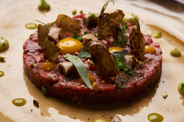 Beef tartare Steak with egg yolk, pistachios, truffle oil, green mayonnaise on porcelain plate. Classic tartare meat with ingredients. Luxury food