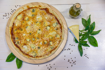 appetizing pizza from four cheeses with olive oil and basil leaves on a white table, flat lay